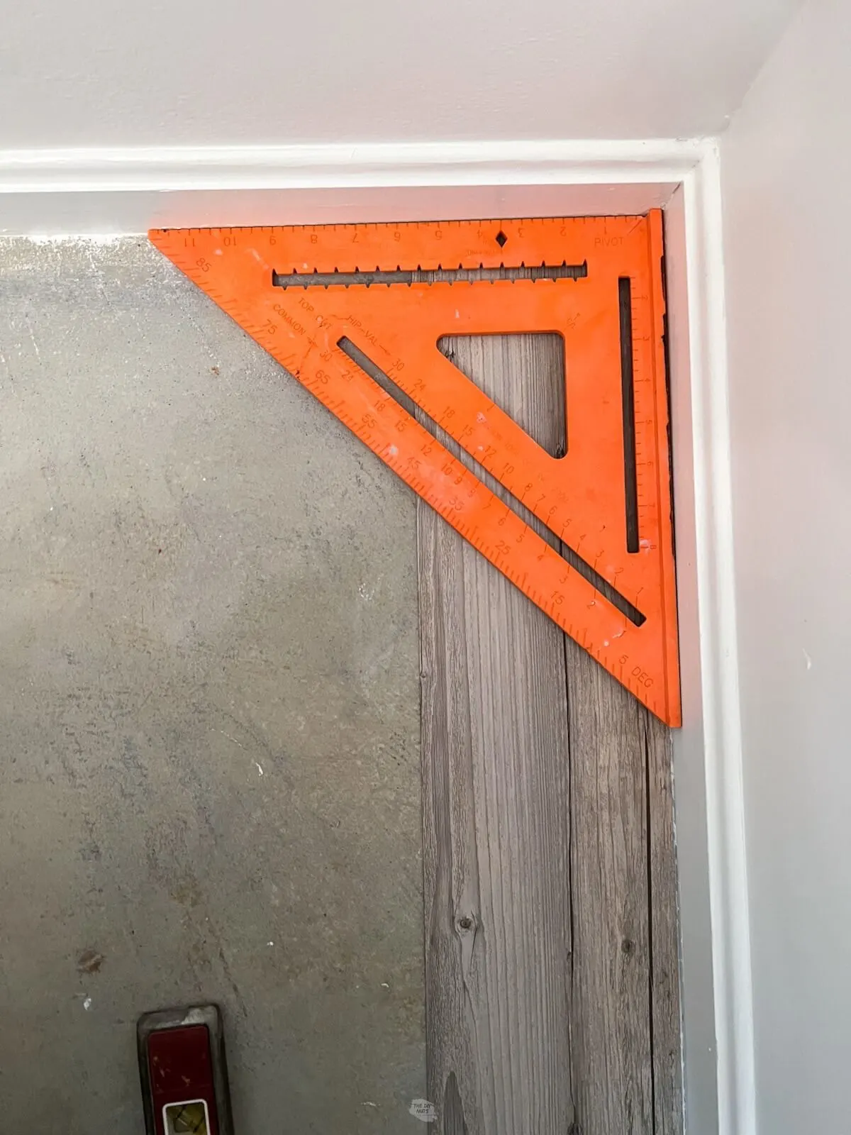 orange speed square in corner of bathroom with concrete and  peel and stick tile on floor.