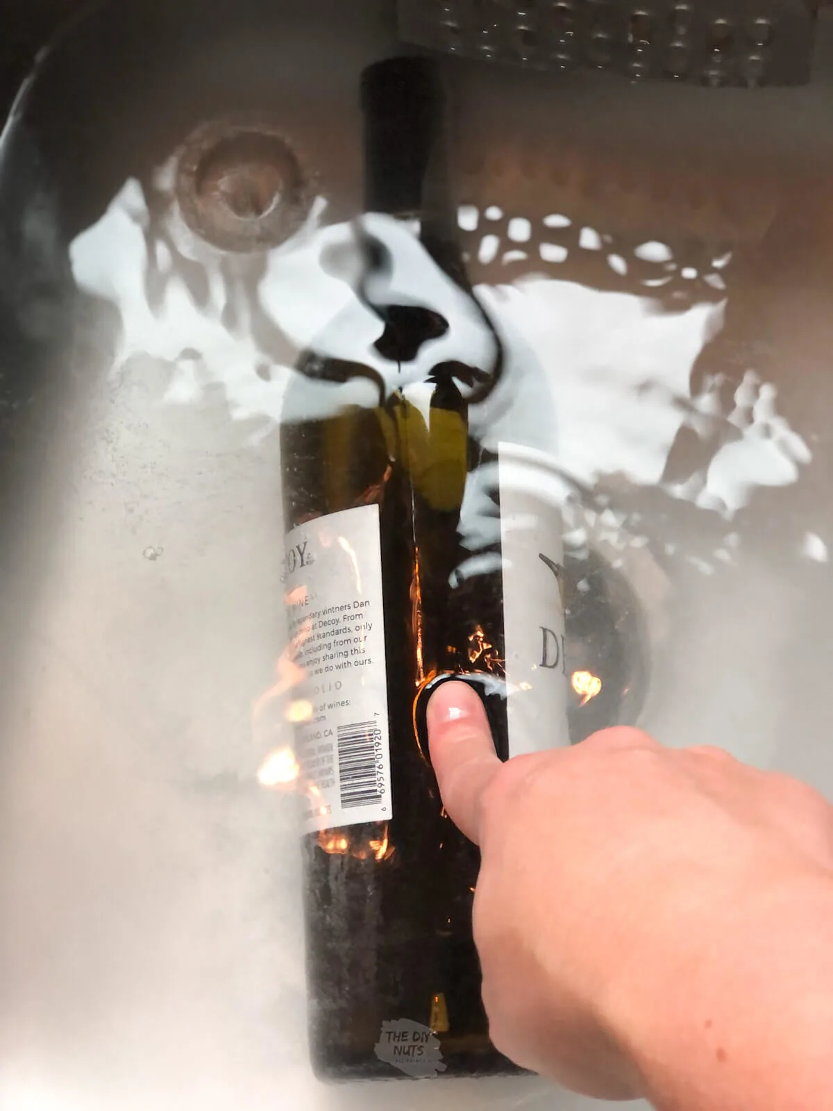 finger pushing wine bottle in baking soda mixture to help get label off