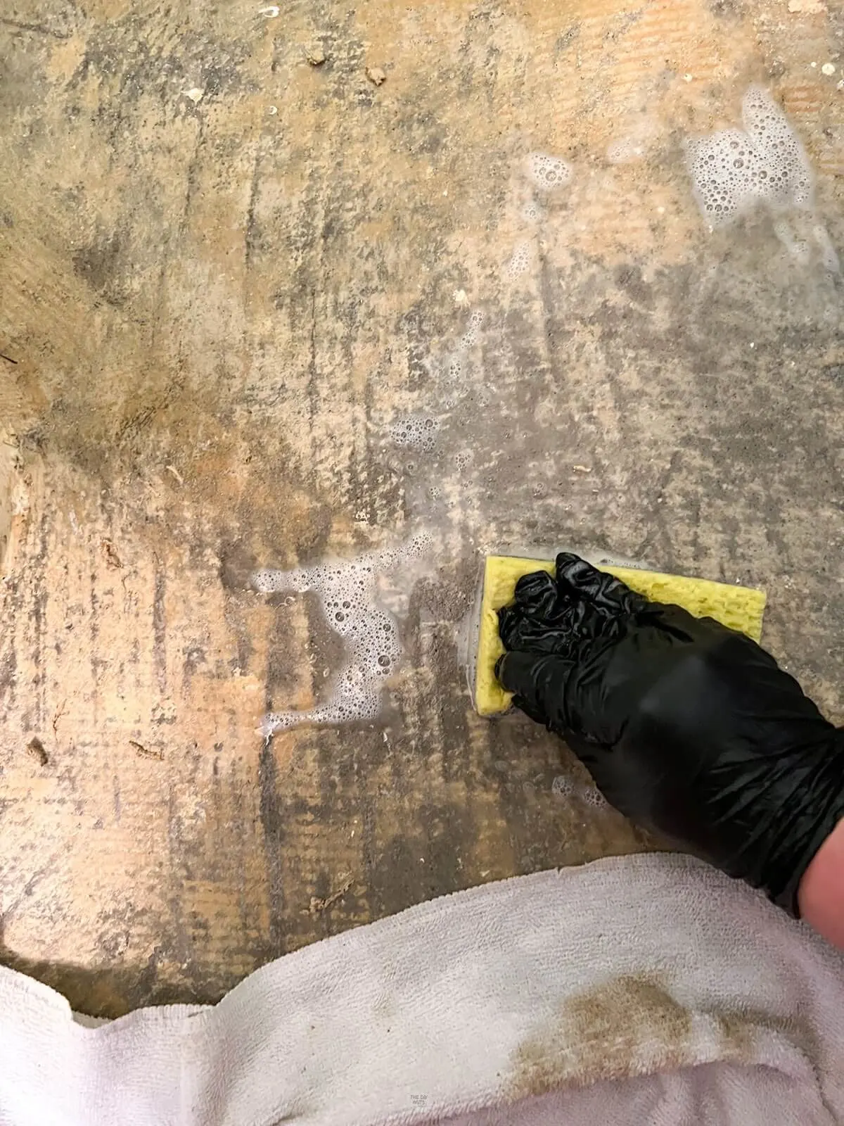 hand wearing glove using yellow sponge to clean floor with carpet glue on it.